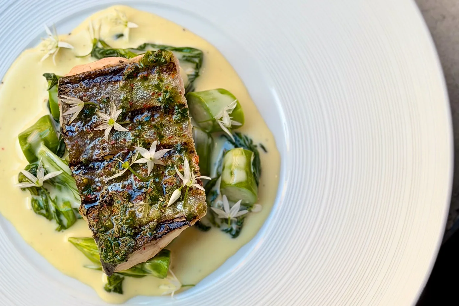 Grillad fisk med grön krusta i gräddsås, med späda grönsaker och vita blommor