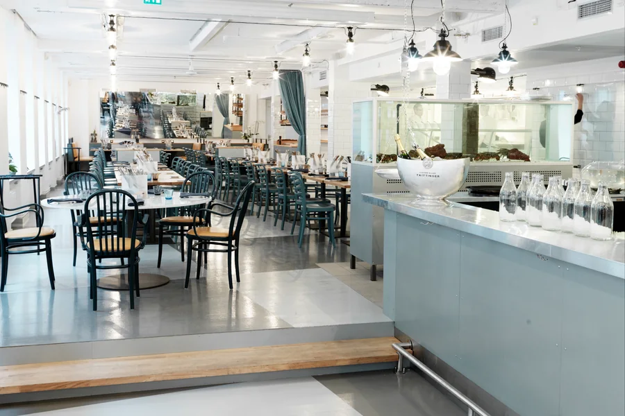 Den större delen med långbord och blågröna trästolar under rader av hängande lampor, med isdisken till höger
