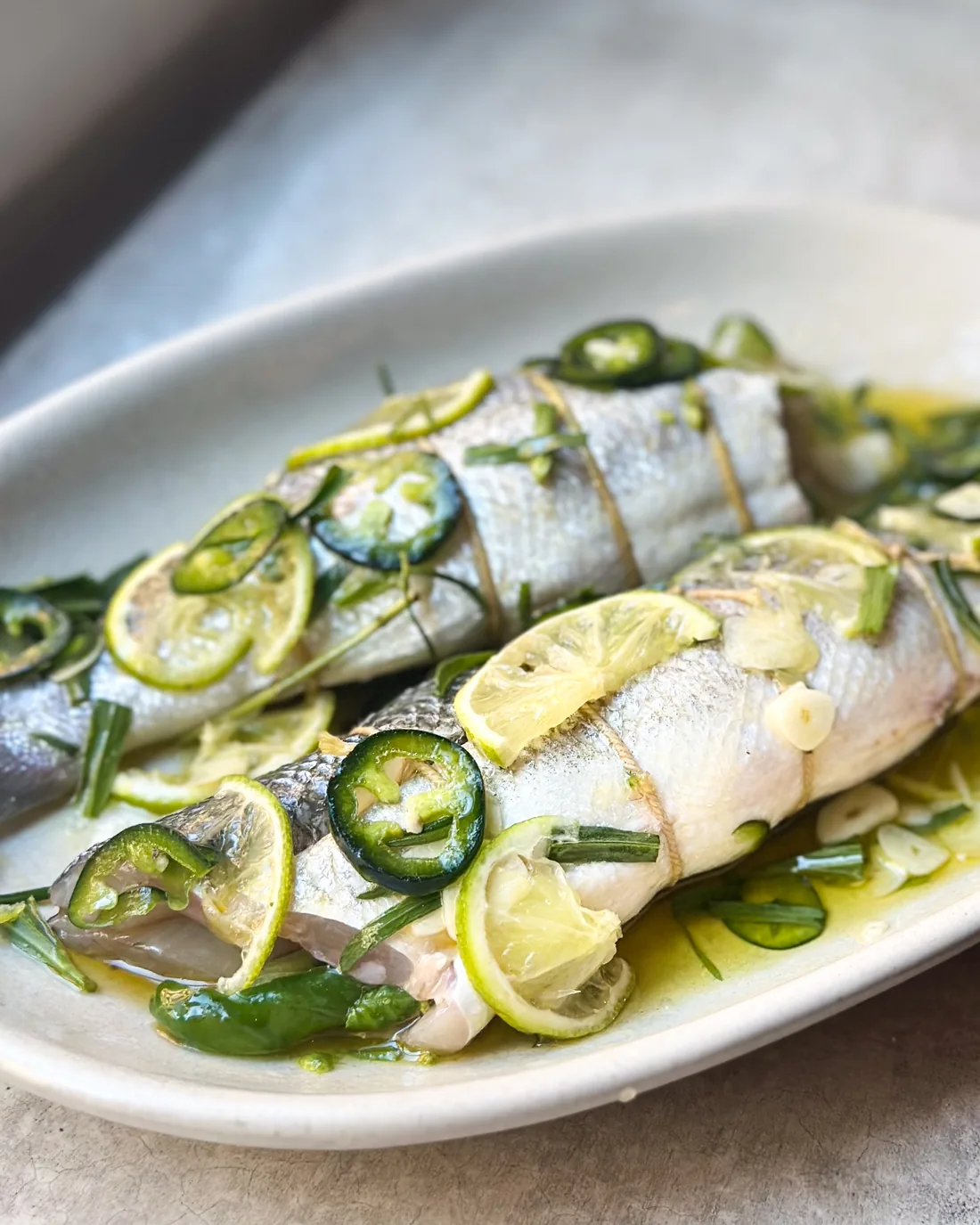 Två hela fiskar med limeskivor, jalapeño och örter på ett avlångt fat