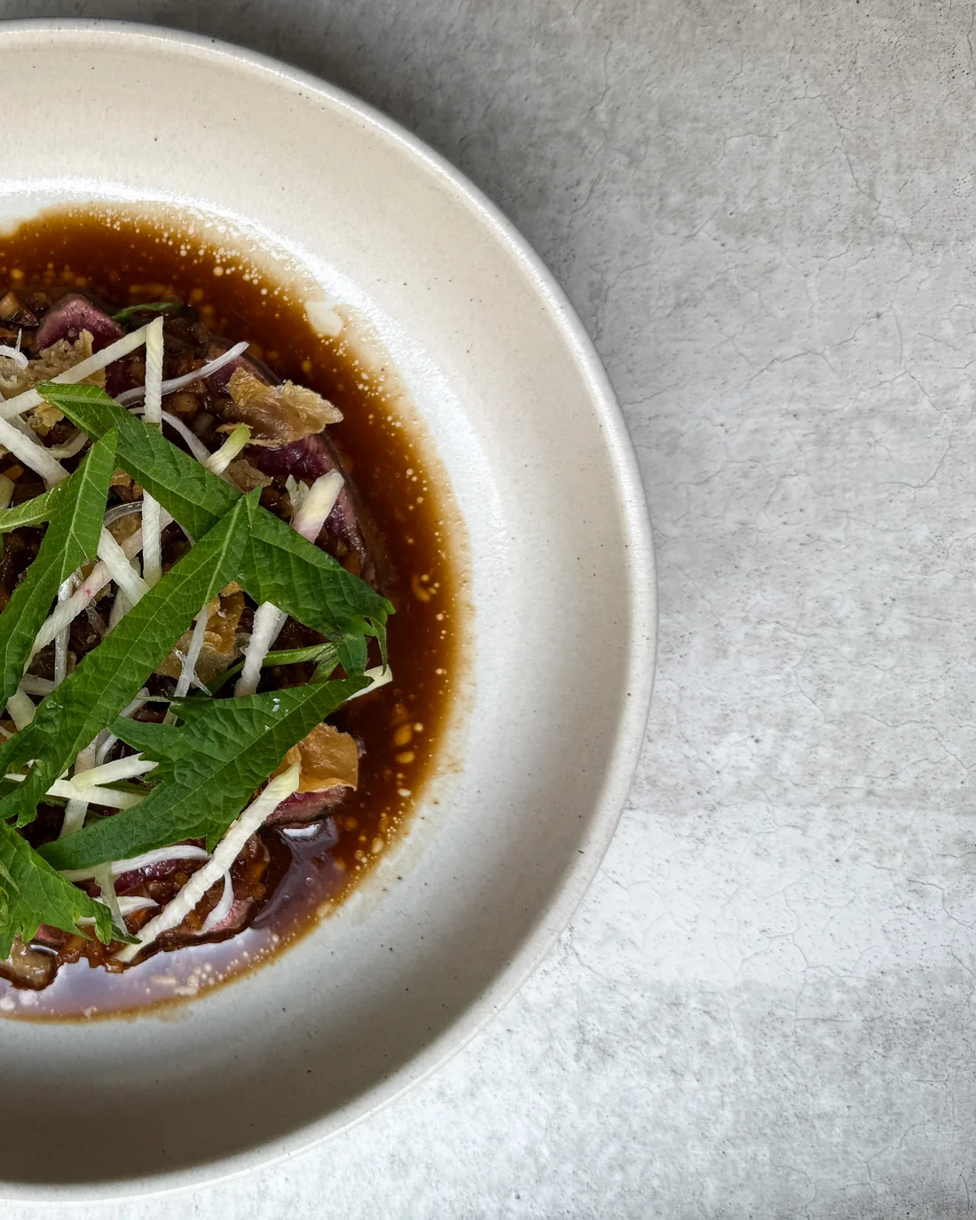 Tartar i mörk buljong med strimlad rädisa och myntablad