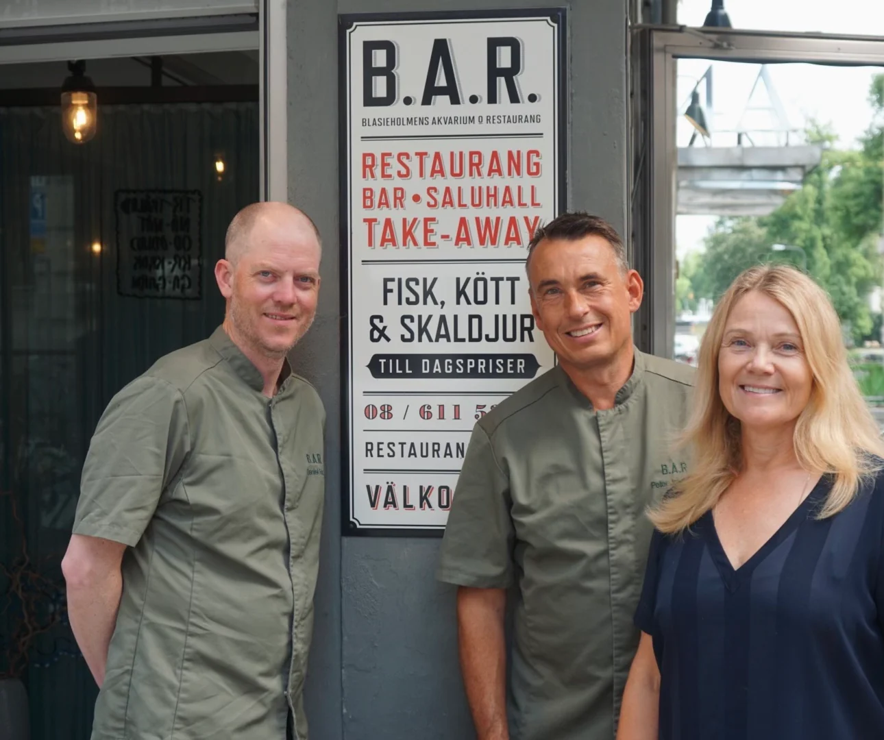 De tre bakom B.A.R. framför entrén, vid den emaljerade skylten som listar restaurang, bar, saluhall och take-away